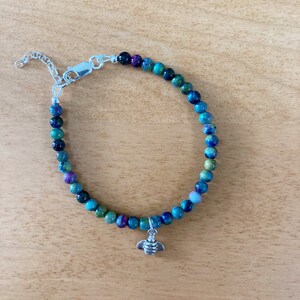 May include: A turquoise and green beaded bracelet with a silver bee charm. The bracelet has a silver clasp.
