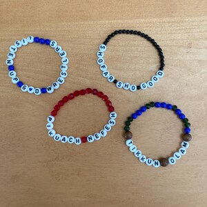 May include: Four beaded bracelets with white letter beads spelling out phrases. One bracelet has blue and white beads, another has black beads, a third has red beads, and the last has blue, green, and brown beads.