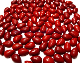 May include: A collection of approximately 70 red coral cabochons in a teardrop shape. The cabochons are polished and have a smooth, glossy finish.
