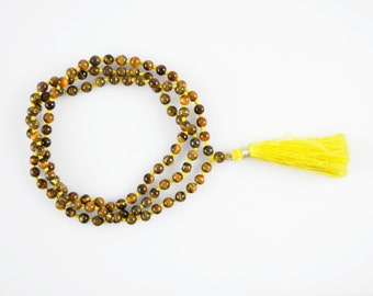 May include: A beaded necklace with tiger eye stones and a bright yellow tassel. The beads are brown and gold, strung on a yellow cord. The tassel is made of yellow threads and is attached to a silver-colored metal piece.