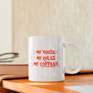 May include: White ceramic coffee mug with the text "MY HOUSE MY RULES MY COFFEE!!" in red lettering. The text is surrounded by small drawings of coffee cups.