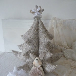 May include: A beige fabric Christmas tree with a white star on top, a beige reindeer ornament, and two white star ornaments. There are also two brown cookies on the white surface.