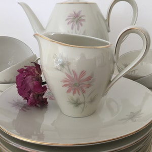 May include: A white tea set with a floral design. The set includes a teapot, creamer, cups, and saucers. The floral design features pink and green flowers.