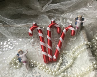 Könnte beinhalten: Drei rote und weiße Zuckerstangen-Weihnachtsbaumschmuck mit einer weißen und silbernen Perlenkette und zwei Porzellan-Engelfiguren.