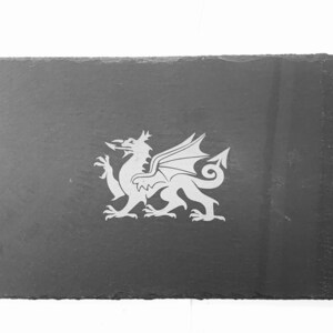 Pode incluir: Um descanso de copo de ardósia preto com um design de dragão galês gravado em branco.