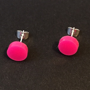 Pode incluir: Um par de brincos de pressão rosa com postes prateados. Os brincos são redondos e têm um acabamento liso e brilhante.