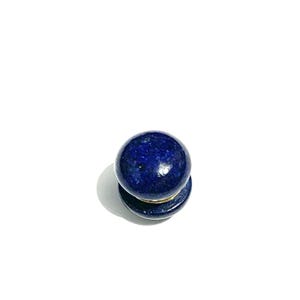 May include: A dark blue lapis lazuli stone, spherical in shape, sits on a matching base. The stone has a polished, glossy finish. The base has a gold-coloured band. The object is on a white background.
