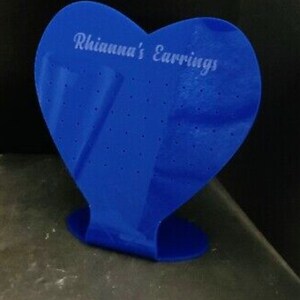 Może przedstawiać: Stojak na kolczyki w kształcie serca w kolorze niebieskim z nadrukiem "Rhianna's Earrings" z przodu.