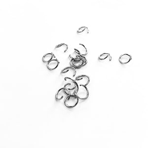 May include: A close-up of a pile of silver jump rings, a type of jewellery finding used for connecting chains, cords, and other jewellery components.