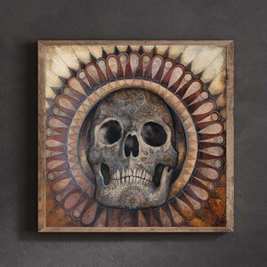 Puede incluir: Obra de arte enmarcada cuadrada que presenta una calavera detallada con intrincados patrones en tonos grises, azules y dorados. La calavera está centrada dentro de un diseño circular de formas de pétalos marrones y rojos, sobre un fondo beige.
