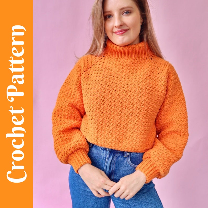 May include: A bright orange crochet sweater with a high neck and long sleeves. The sweater has a textured stitch pattern and is cropped.