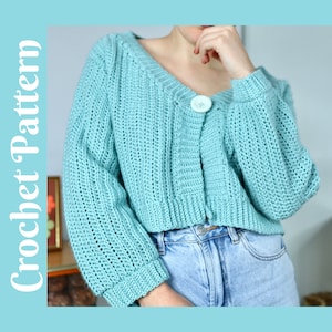 以下が含まれることがあります： ボタン留めの長袖の薄いブルーのクロシェカーディガン。カーディガンは丈が短く、ややゆったりとしたシルエットです。