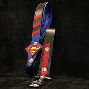May include: A blue and red leather dog lead with a Superman logo. The lead has a black leather handle and a silver clip.