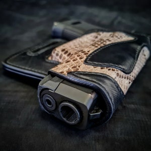 Op de afbeelding: Een zwart leren pistoolholster met een slangenhuidpatroon. Het holster is ontworpen om te passen bij een pistool met een loop en een magazijn.