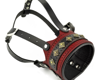 May include: A red leather dog muzzle with black leather straps and gold-toned accents. The muzzle has a decorative design with small squares and a band of gold-toned studs.