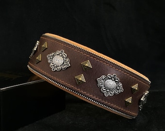 May include: A brown leather dog collar with decorative metal accents. The collar has a zipper closure and is adorned with ornate metal medallions and pyramid-shaped studs.