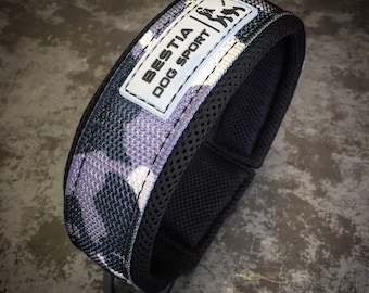 May include: A black and gray camouflage dog collar with a white label that says "BESTIA DOG SPORT".