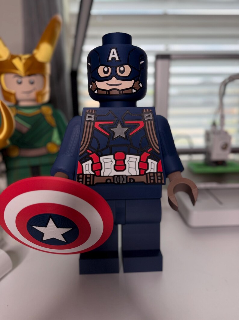 May include: A Captain America action figure in a block style, holding a red, white, and blue shield with a white star. The figure is dark blue with red and white accents and a helmet with the letter "A". Another figure is visible in the background.
