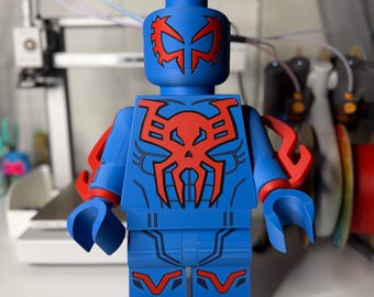May include: A large blue figurine resembling a Lego figure, featuring red accents. The figure has a detailed design on the head, chest, and legs, with red arm attachments. The overall design is reminiscent of a superhero.