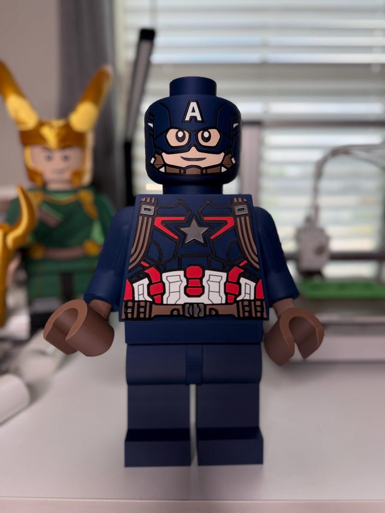 May include: A Captain America Lego figure, primarily navy blue, with a white "A" on the helmet. The figure has a star on the chest and brown hands. Another Lego figure, Loki, is visible in the background.
