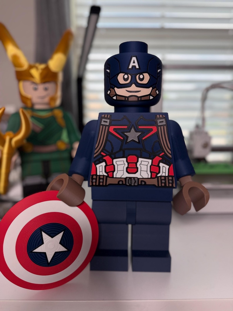 May include: A Captain America Lego figure, featuring a blue and red costume with a star emblem and a matching shield. The figure has a blue helmet with the letter "A" and brown arms. Another Lego figure of Loki is visible in the background.