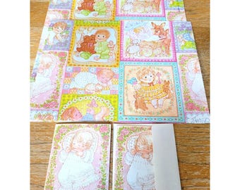 May include: A collection of vintage-style stationery featuring a large sheet of wrapping paper and two matching greeting cards with envelopes. The paper displays a grid of pastel illustrations showing babies, deer, and rabbits in floral frames.