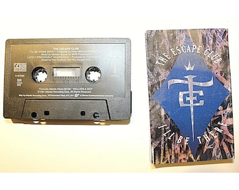 May include: A black cassette tape and its paper insert for The Escape Club single I'll Be There. The tape features white text detailing track information and Atlantic Records branding. The insert displays a blue diamond logo with a crown icon.