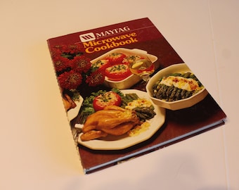 May include: A vintage Maytag Microwave Cookbook with a red cover featuring a photo of a roasted chicken, asparagus, and stuffed tomatoes.