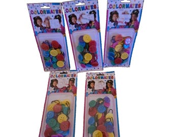 May include: Five packages of Colormates buttons, each containing an assortment of round, multi-colored plastic buttons attached to black elastic loops. The packaging features the brand name Colormates at the top and images of children.