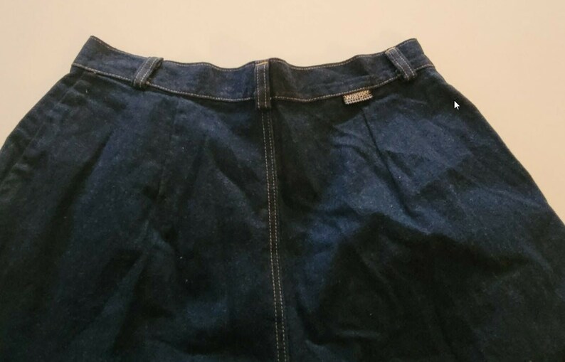 May include: A dark blue denim skirt with a center seam and a small label on the back waistband.