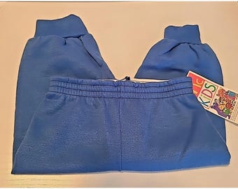 May include: Solid blue sweatpants featuring an elastic waistband and ribbed cuffs at the ankles. A rectangular white tag is attached to the side, displaying the text "McKids" in colorful letters alongside a graphic illustration of various cartoon characters.