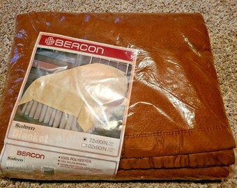 May include: A brown Beacon Salem blanket packaged in plastic. The label reads "Salem Blanket" and lists the sizes 72x90in. and 102x90in. The label also states that the blanket is 100% polyester with a 100% nylon binding.