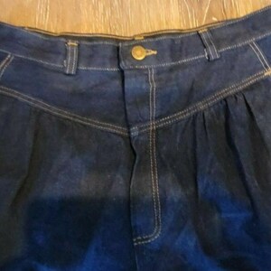 May include: A pair of dark blue denim high-waisted pants with a button closure and a pleated front.