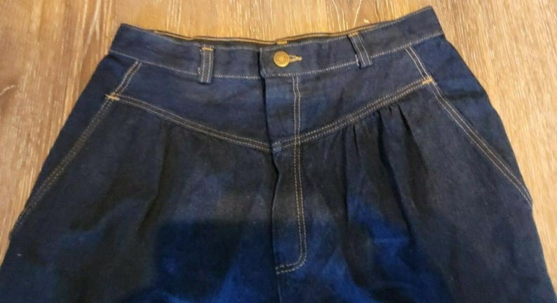 May include: A pair of dark blue denim high-waisted pants with a button closure and a pleated front.