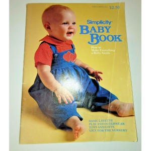 May include: A Simplicity Baby Book with a yellow cover featuring a baby wearing a red polka-dot shirt and blue overalls with heart appliques. The text reads Simplicity Baby Book, How to Make Everything a Baby Needs, Basic Layette, Play and Outerwear, Toys and Gifts, Nice for the Nursery.