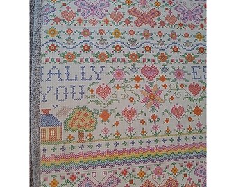 May include: A white fabric sampler featuring colorful cross-stitch embroidery. The design includes repeating rows of butterflies, hearts, flowers, and a small house with a tree. The text "ALLY YOU" is stitched in blue letters on the left side.
