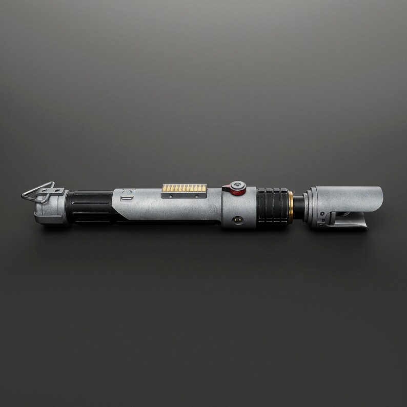 Peut inclure: Un sabre laser argent&eacute; et noir avec un bouton rouge et un d&eacute;tail dor&eacute;. Le sabre laser a une poign&eacute;e noire et une lame argent&eacute;e.