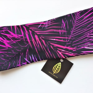May include: A black headband with a pink and purple palm leaf print. The headband has a tag attached that says "www.ecograin.com".