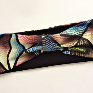 May include: A black headband with a colorful patterned fabric bow. The fabric has a geometric design with blue, pink, gold, and brown colors. The headband has a label that says "eko-banz".