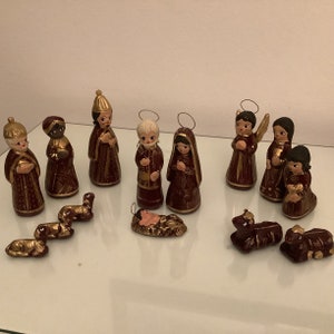 May include: A nativity scene set with 12 ceramic figurines, including the baby Jesus, Mary, Joseph, three wise men, three shepherds, an angel, and two sheep. The figurines are painted in shades of brown and gold, with intricate details.