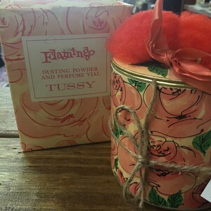 May include: A vintage TUSSY Flamingo dusting powder and perfume vial with a pink rose pattern. The container is tied with twine and topped with a red fluffy puff.