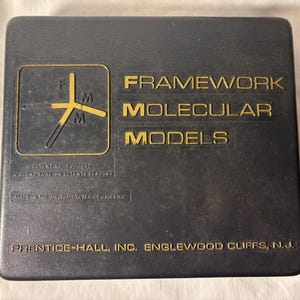 May include: Black plastic case with gold lettering that reads "Framework Molecular Models". The case has a small gold logo with the letters "F", "M", and "M" in a triangular shape.
