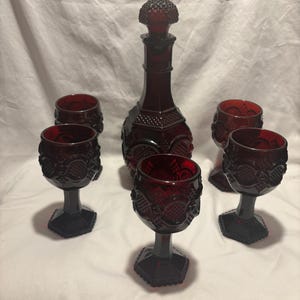 Puede incluir: Un juego de seis copas de vino de vidrio rojo y una jarra a juego. Las copas y la jarra tienen un patrón texturizado en forma de diamante.