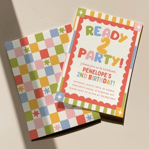 May include: A rectangular birthday invitation and matching envelope featuring a colourful checkerboard pattern with small star icons. The invitation displays the text READY 2 PARTY! and details for Penelope's 2nd birthday celebration in a scalloped border.