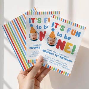 Pu&ograve; includere: Un gruppo di inviti di compleanno colorati. Gli inviti presentano il testo "IT'S FUN to be ONE!" con una foto di un bambino con un cappello da festa. Gli inviti hanno un design a righe arcobaleno.