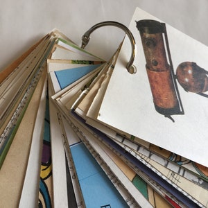 May include: A vintage-style, brown and black telescope with a brass-colored ring on a white background. The telescope is on a wooden stand with a round base. The telescope is part of a fan-shaped collection of cards held together by a silver ring.