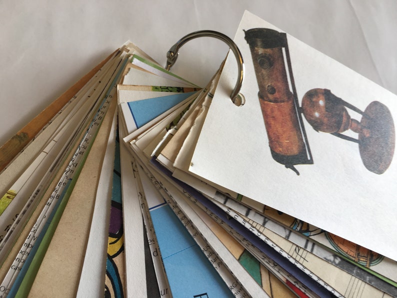 May include: A vintage-style, brown and black telescope with a brass-colored ring on a white background. The telescope is on a wooden stand with a round base. The telescope is part of a fan-shaped collection of cards held together by a silver ring.