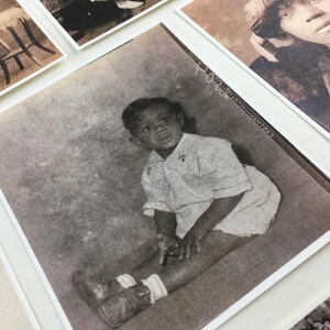 May include: A black and white photograph of a young boy sitting on the floor. He is wearing a light-colored shirt and has a serious expression on his face.