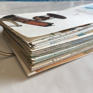 May include: A stack of vintage postcards bound together with a silver ring binder. The top card features a drawing of a vintage lamp.