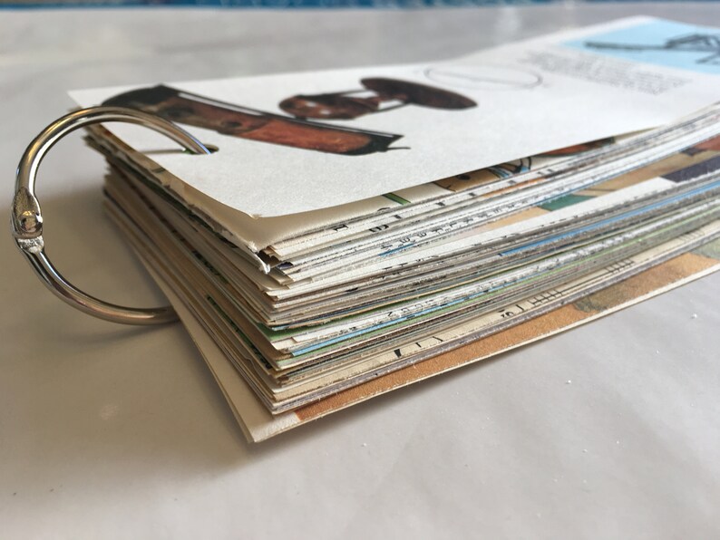 May include: A stack of vintage postcards bound together with a silver ring binder. The top card features a drawing of a vintage lamp.